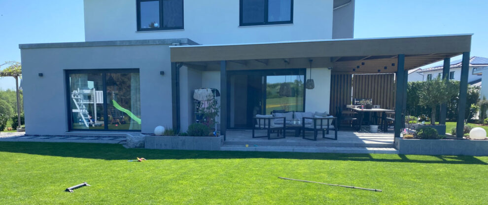 Moderner Außenbereich eines Einfamilienhauses mit überdachter Terrasse, Lounge-Möbeln, Essbereich und großem Garten.