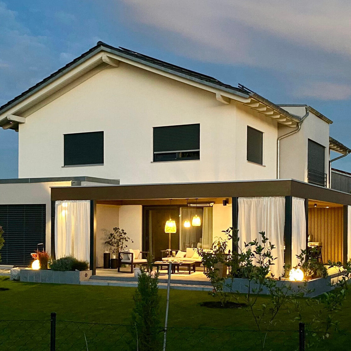 Modernes Einfamilienhaus mit beleuchteter Terrasse und Garten in stimmungsvoller Abendatmosphäre.
