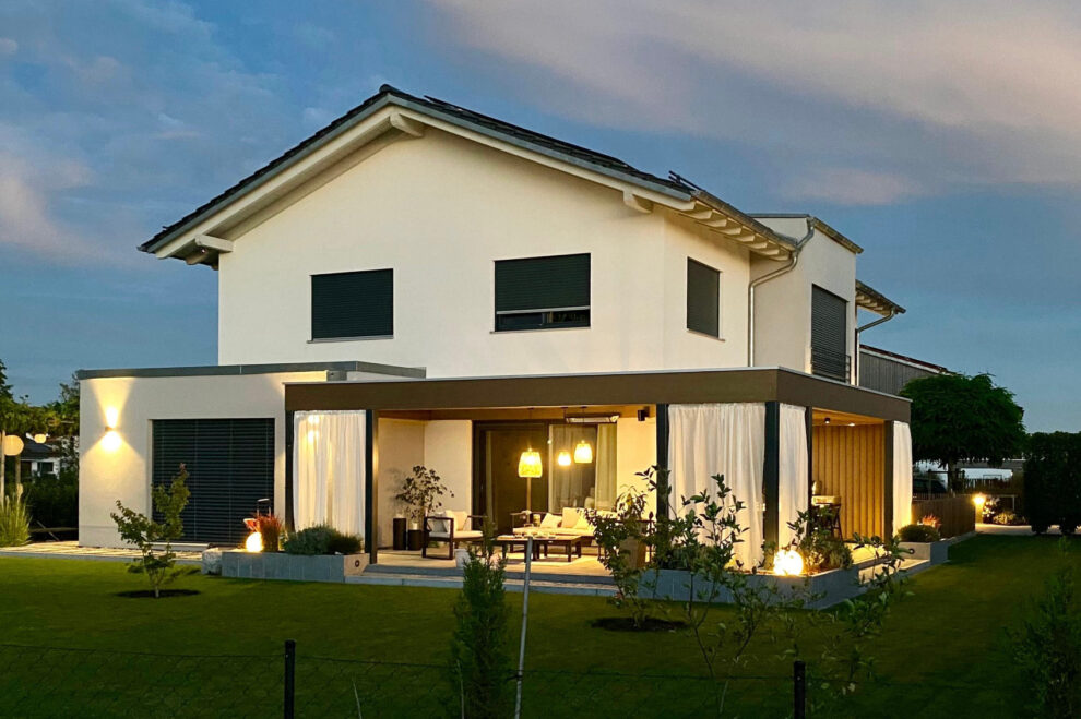 Modernes Einfamilienhaus mit beleuchteter Terrasse und Garten in stimmungsvoller Abendatmosphäre.